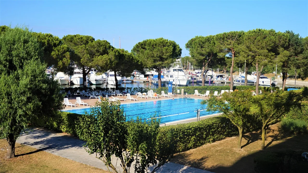 Grande piscina condominiale tra i pini con la darsena sullo sfondo