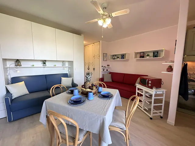 Soggiorno con divano blu, tavolo apparecchiato e ventilatore a soffitto