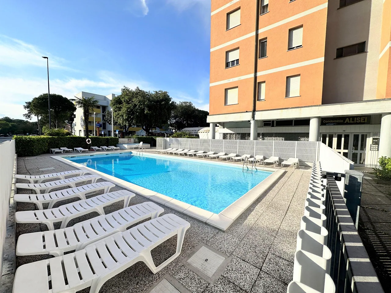 Piscina condominiale con lettini bianchi e cielo terso