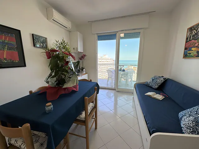 Soggiorno con tavolo apparecchiato, divano blu e portafinestra sul mare
