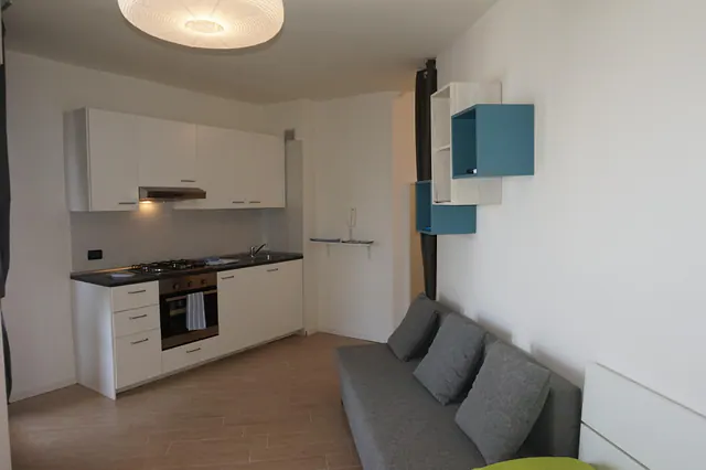 Monolocale con cucina bianca e divano grigio