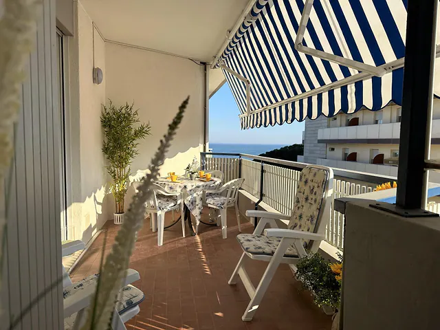 Terrazzo con tenda a righe, tavolo e sdraio con scorcio di mare