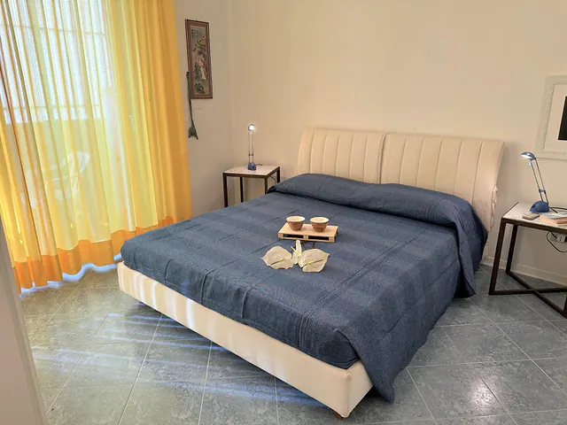 Camera matrimoniale con copriletto blu e tende gialle