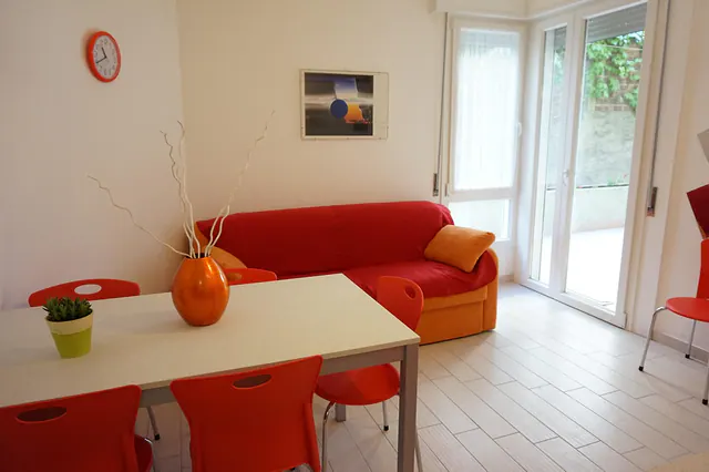 Soggiorno luminoso con divano rosso e portafinestra sul patio
