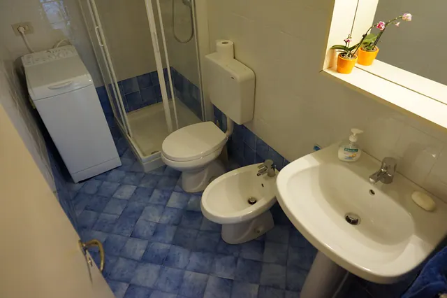 Bagno con box doccia, lavatrice e piastrelle blu