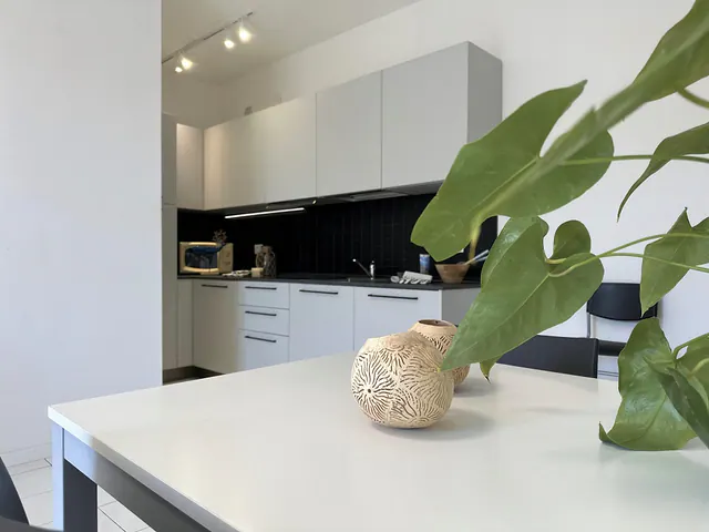 Cucina bianca con rivestimento scuro e tavolo in primo piano