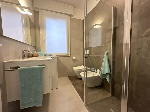 Bagno con doccia in vetro e rivestimento effetto pietra